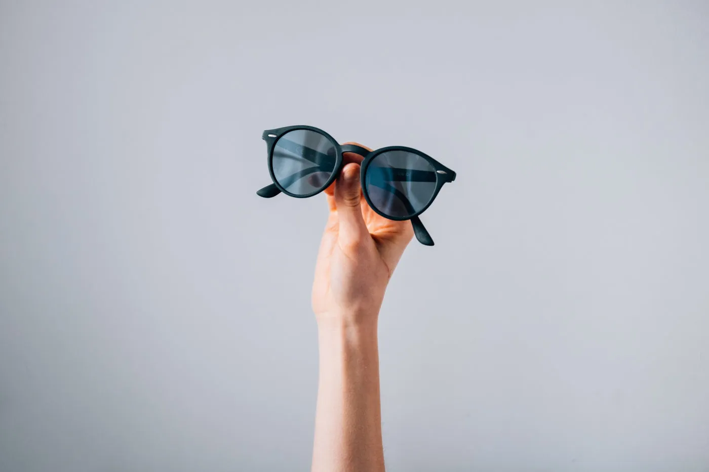 Pair Of Sunglasses Held In Front Of Grey Background